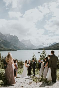 a group of people standing around each other in front of a body of water with mountains in the background