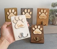 a person holding up three wooden magnets with dog's name and paw prints on them