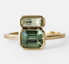 an engagement ring with two green stones on it's sides, one in yellow gold and the other in white gold