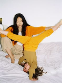 two women are laying on the bed and one is reading a book