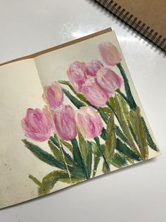 a drawing of pink tulips is shown on a white surface next to a spiral notebook