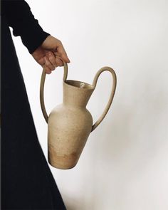 a person holding a vase in their left hand while standing next to a wall with a white background