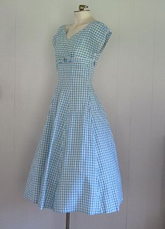 DESCRIPTION 1950s cotton dress Blue and white gingham Wide v-neck embellished with rhinestones and beads Under bust bow Fitted bodice/waist and full skirt Hand made Narrow white rick rack trim APPROXIMATE MEASUREMENTS (INCHES): Bust: 33 Waist: 26 Hip: OPEN Bodice (shoulder to waist): 15 Skirt (waist to hem): 30 CONDITION Excellent/very good. The under arms on both sleeves have been repaired/reinforced. Aside from this, the dress appears unworn. 1950s Cotton Dress, 1950s Country Fashion, Vintage Gingham Dress, 1950s House Dress, Cotton V-neck Dress For Picnic, Vintage Dresses 50s Casual, 1950s Style Gingham Cotton Dress, Vintage Blue Dress For Picnic, Blue Vintage Dress For Picnic