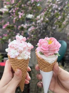 two ice cream cones with pink and white flowers on top, in front of a flowering tree