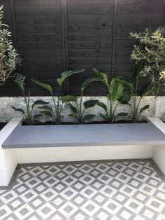 an outdoor bench with plants growing on it in front of a wall and tiled floor