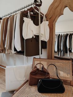 clothes and handbags are hanging on racks in a clothing store, while a woman's purse sits next to it