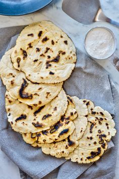 homemade pita breads on a towel next to a bowl of flour and spoon