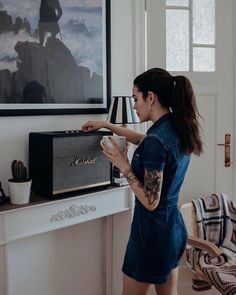 a woman standing in front of a table with a radio on top of it and holding a cup