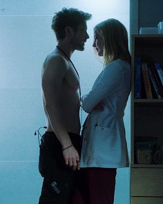 a man and woman standing next to each other in front of a book shelf with books on it