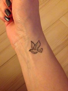 a woman's wrist with a small bird tattoo on the left side of her arm