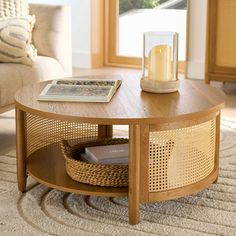 a coffee table with a basket underneath it and a candle on the top, in front of a window