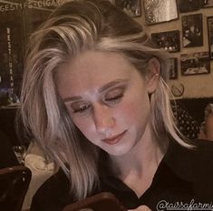 a woman looking at her cell phone while sitting in a restaurant with pictures on the wall behind her