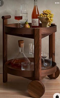 a wooden table topped with bottles and glasses next to a vase filled with fruit on top of a hard wood floor