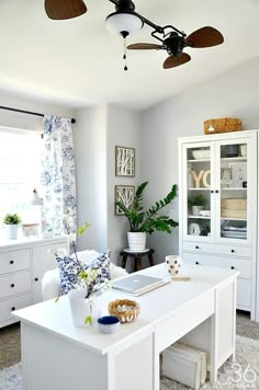 an image of a room with white furniture and decor on the walls, including a ceiling fan