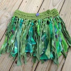 a green crocheted skirt with fringes on top of a wooden floor next to a piece of wood