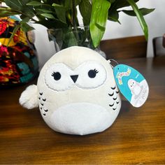 an owl stuffed animal sitting next to a potted plant on a wooden table with a tag