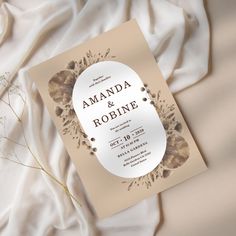 an elegant wedding card is laying on the bed with white linens and dried flowers