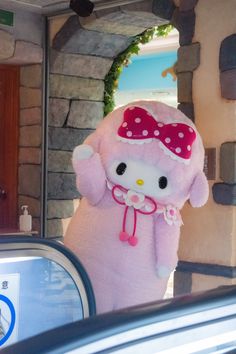 a hello kitty stuffed animal is standing in front of a door with a pink bow on it's head