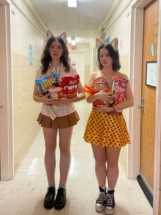 two girls in costumes holding candy bags and standing next to each other on a hallway