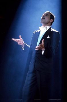 a man in a tuxedo standing on stage with his hands out to the side