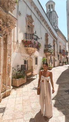 a woman is walking down the street in an old european town, wearing a white dress