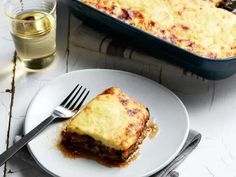 a piece of lasagna on a plate next to a glass of water and fork