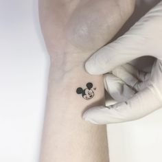 a person's wrist with a small mickey mouse tattoo on the left side of their arm