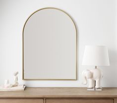 an oval mirror on a wall above a dresser with a lamp and elephant figurine