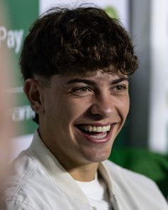 a young man smiling and wearing a white shirt in front of a green sign that says pay