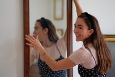 a woman standing in front of a mirror holding her arm up to the side with one hand