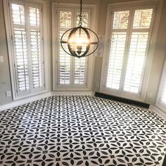 a black and white patterned floor in an empty room with shutters on the windows