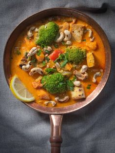 a pan filled with soup and vegetables on top of a table next to a slice of lemon