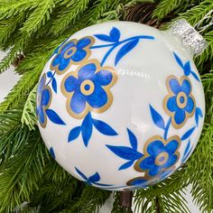 a blue and white ornament sitting on top of a green christmas tree branch