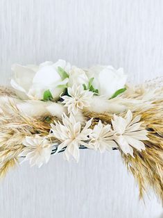 some white flowers are sitting in a vase with grass and feathers on it's side