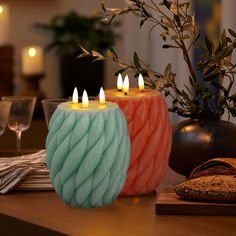 two candles sitting on top of a wooden table next to bread and wine glasses