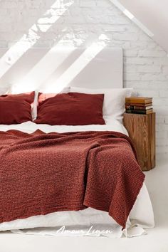 a bed with red pillows and blankets in a white room next to a brick wall