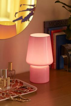 a pink lamp sitting on top of a table next to a mirror and other items