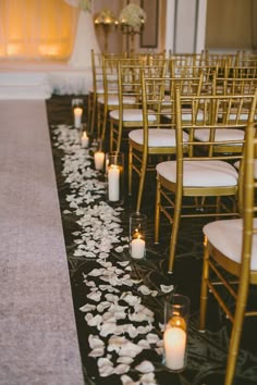 rows of chairs with white flowers on the floor and candles lining the aisle in front of them