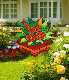 a flower pot sitting in the middle of a garden with flowers around it and a house behind it