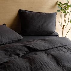 a bed with black linens and pillows on top of it, next to a potted plant