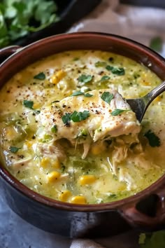 a spoon full of chicken and corn soup with cilantro on the side, ready to be eaten