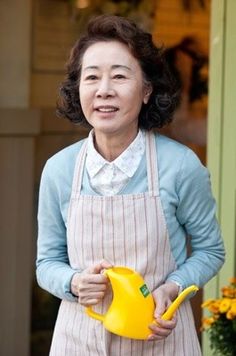 an older woman holding a yellow watering can