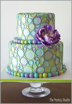 a three tiered cake decorated with circles and a purple flower on the top layer