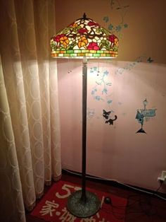 a floor lamp with a stained glass shade on it in front of a curtained window