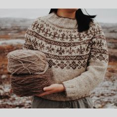 a woman holding a ball of yarn in her hands and wearing a sweater with an ornament pattern