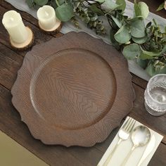 a wooden table topped with a brown plate and two silverware next to greenery