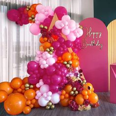 a birthday cake made out of balloons and streamers in front of a pink backdrop