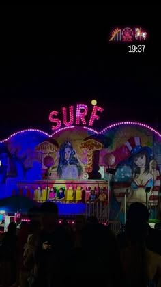 people standing in front of an amusement park at night with neon signs and lights on the building