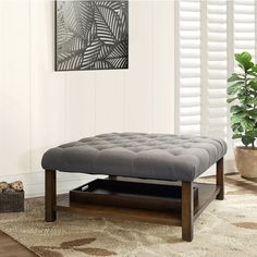 a living room with a gray ottoman and white rug on the floor next to a potted plant