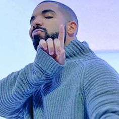 a man in a blue sweater holding his hand up to his face and making the peace sign